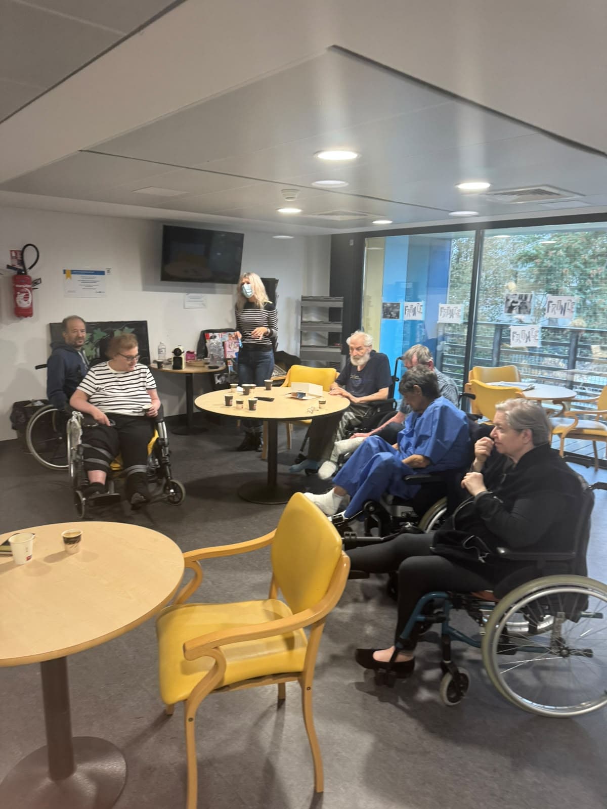 Deux visiteuses bénévoles dansent devant des patients installés autour de tables dans une salle hospitalière.