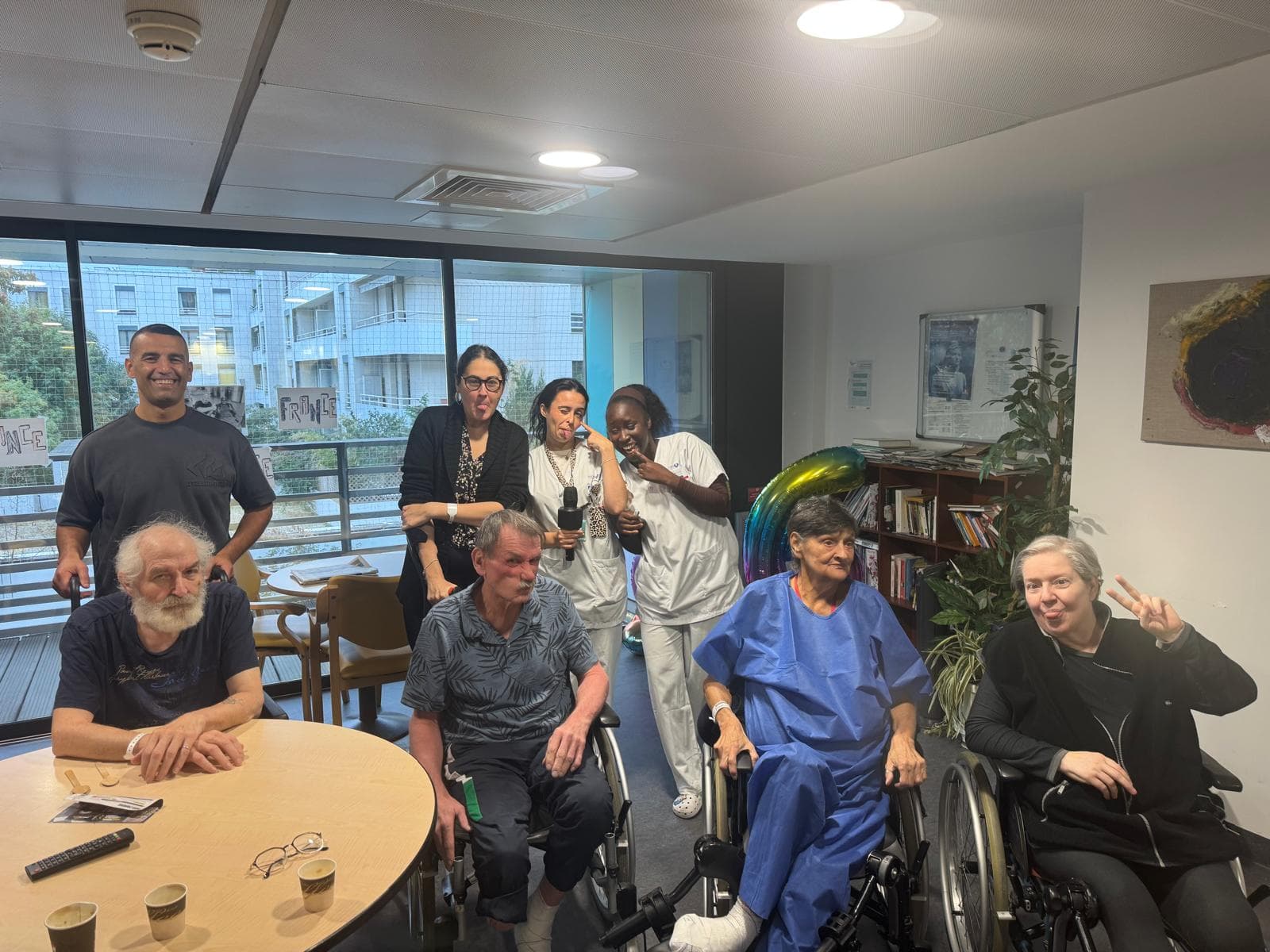 Jeunes bénévoles, soignants et patients posent ensemble dans la salle de convivialité d'un service.
