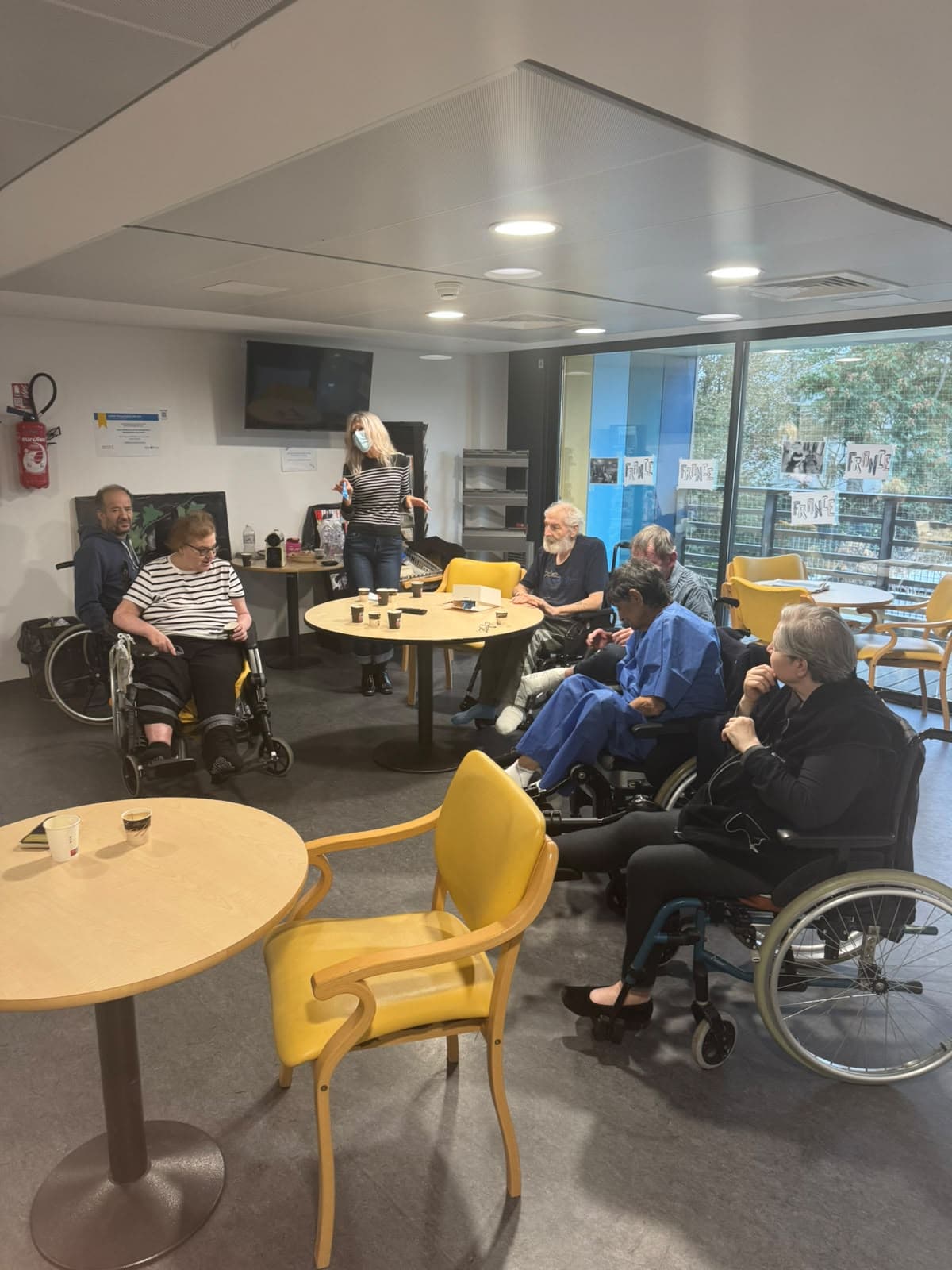 Patients et bénévole en discussion autour d'une table ronde dans un service hospitalier.